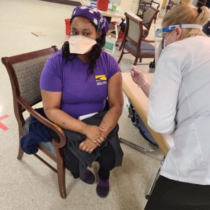 Изображение caregiver в футболке SEIU 775 и маске, получающей вакцину от COVID
