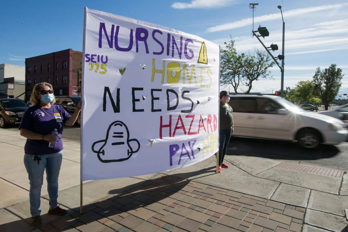 Caregivers Nelly Prieto, left, and Brenda Cuevas hold a large sign during a protest for facility funding and hazard pay for nursing home workers Thursday, June 18, 2020, in downtown Yakima, Wash.