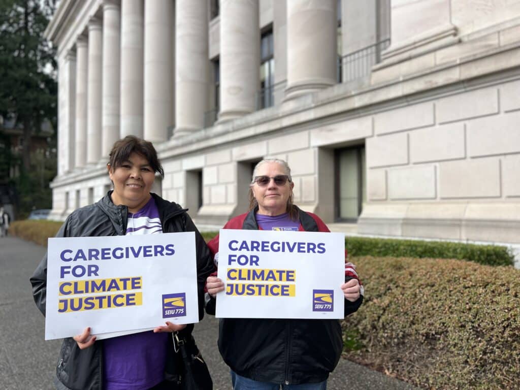 Two people hold signs that say "Caregivers for climate justice"